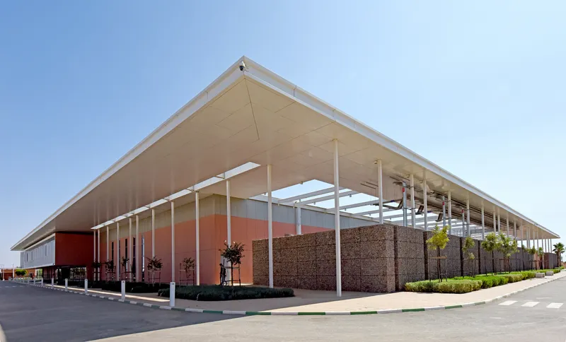 Oblique view of the cantilevered roof with white columns and gabion base under clear skies