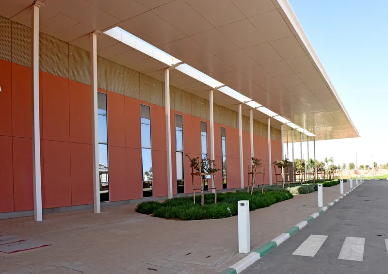 Entry facade with terracotta panels and vertical windows beneath a deep overhanging roof with planted beds