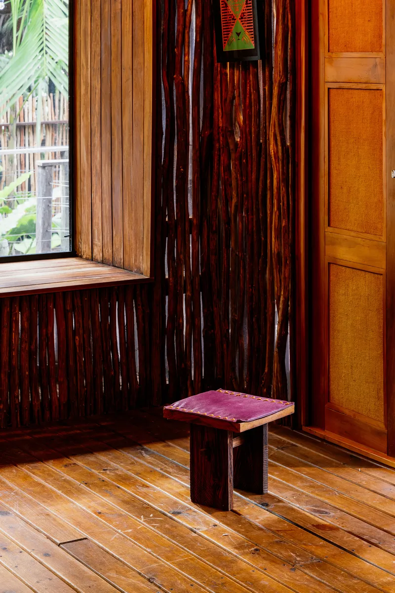 Corner detail with a low timber stool on plank flooring beside bundled bamboo walls