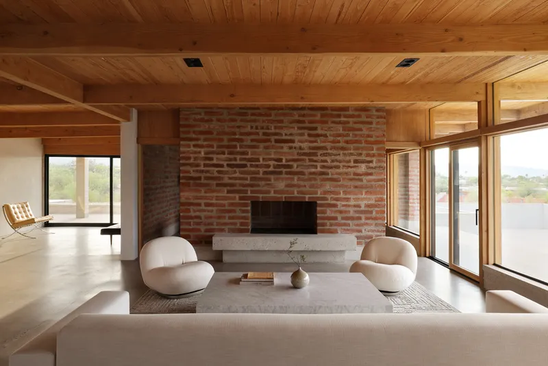 Red brick fireplace wall with concrete hearth beneath a timber plank ceiling with exposed beams