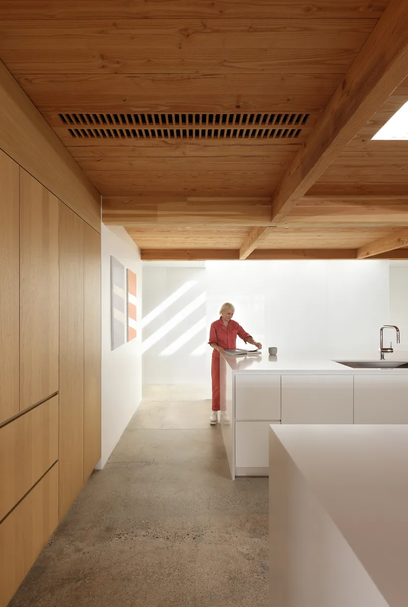 Kitchen with slatted timber ventilation grille inset in ceiling and person in red standing at island counter