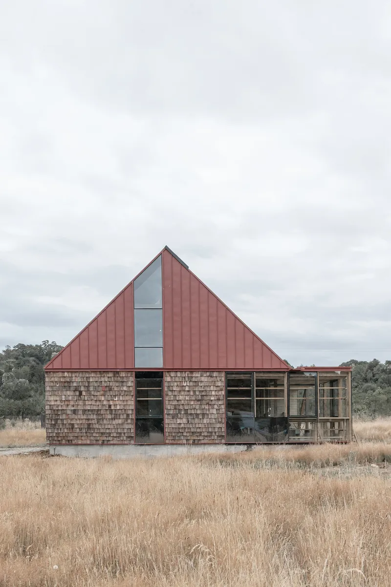 Side elevation showing the red metal roof, vertical glazing slot, and enclosed terrace under overcast skies