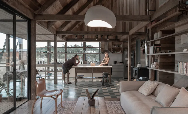 Open-plan living area with exposed timber beams, patterned floor tiles, and two people at the island