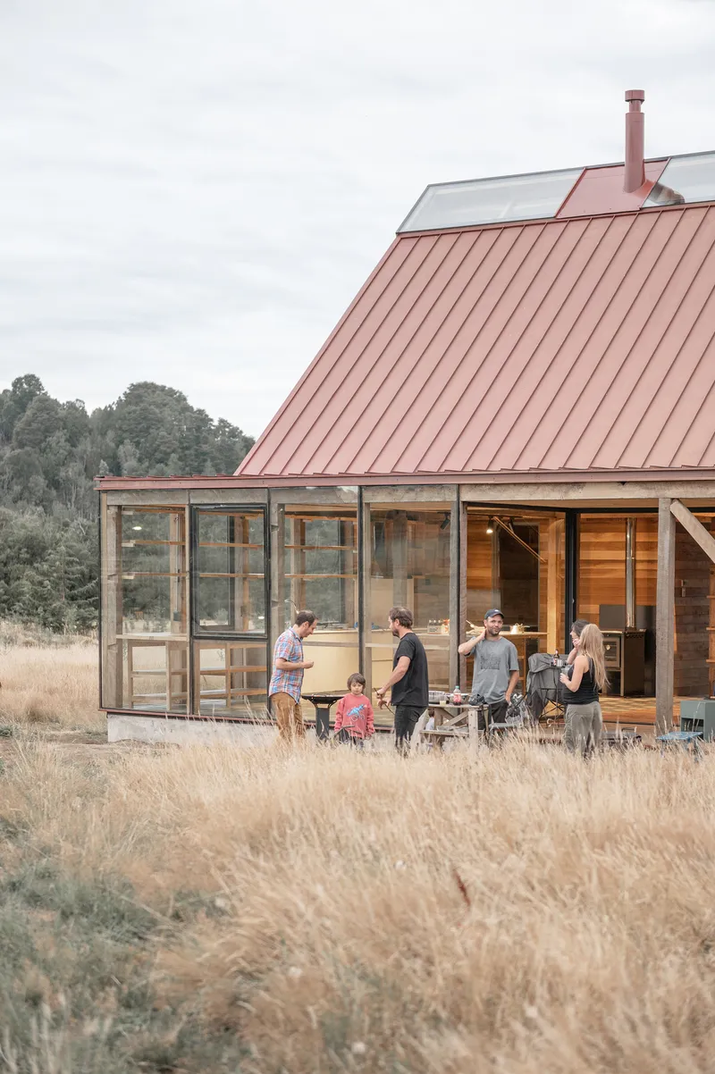 Glazed terrace and red metal roof with a family gathered on the deck in golden hour light