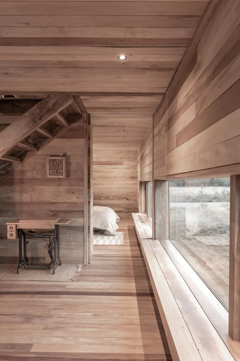 Horizontal timber-lined bedroom with a low window bench and staircase rising to the upper level
