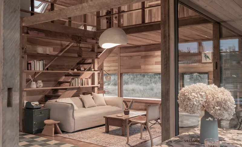 Double-height living space with timber-clad walls, open timber staircase and floor lamp beside a sofa