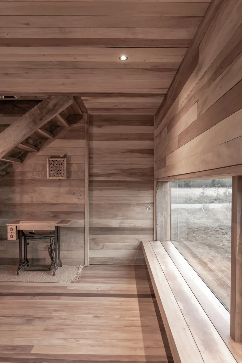 Timber-lined interior showing a built-in bench beside a wide horizontal window and exposed staircase