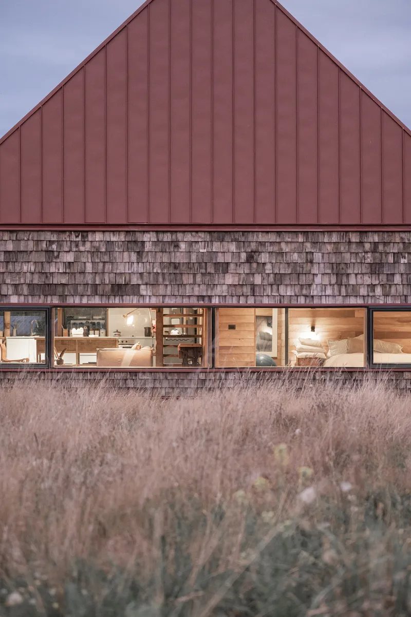Facade detail showing horizontal band of windows between shingle cladding and red metal roof at twilight