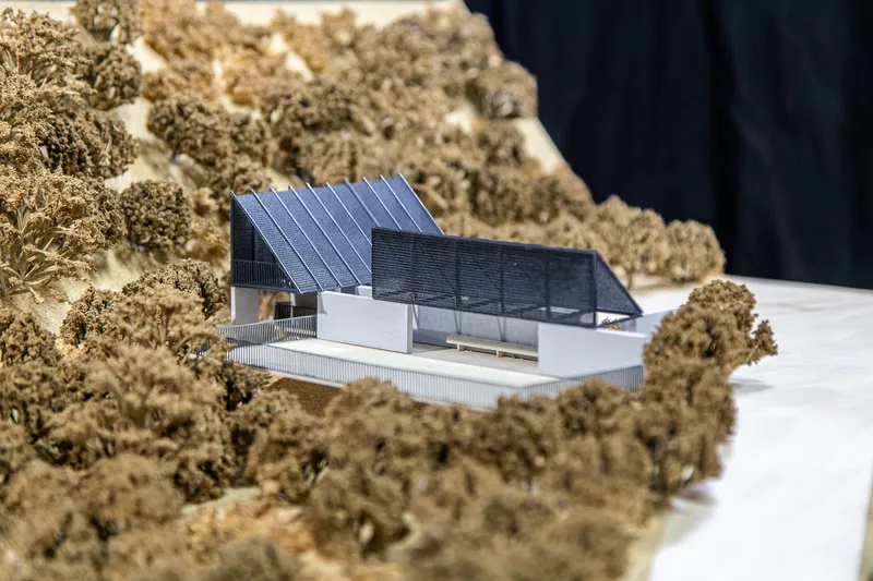 Physical model showing slatted facade and angled roof volumes embedded in wooded terrain