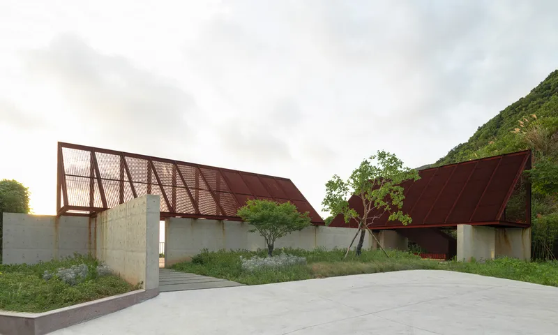 Entry view of angled roofs with corrugated metal screens over concrete walls and planted beds