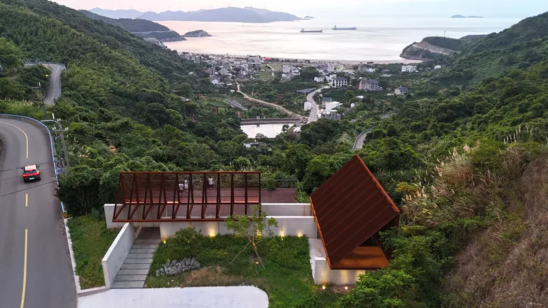 Aerial view of two tilted roof volumes on a hillside overlooking the bay at dusk
