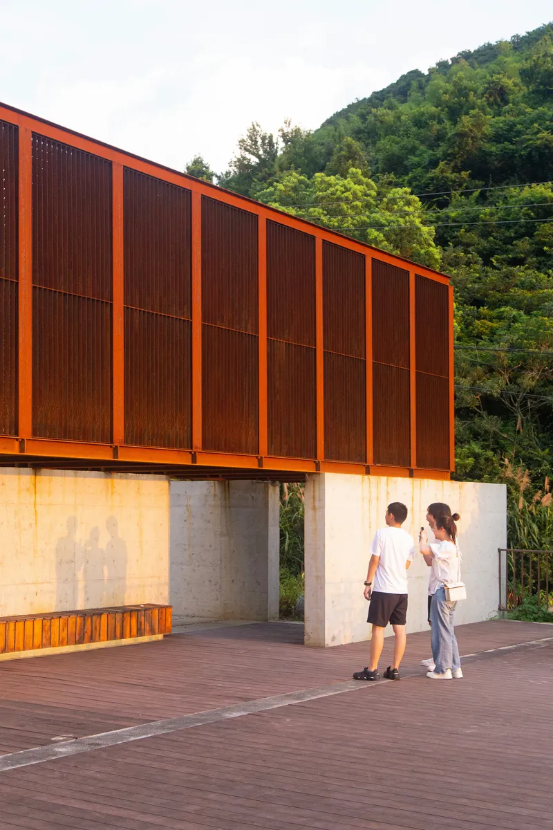 Concrete columns supporting a cantilevered volume with vertical metal screens, two visitors standing beneath