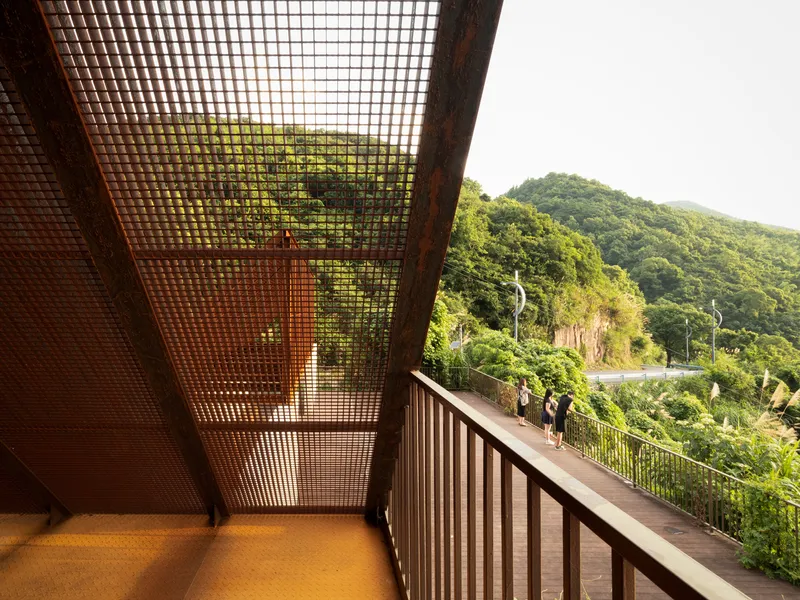 Interior balcony view through a corrugated metal mesh ceiling toward the forested hillside