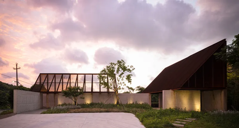 Street view of the angled timber and concrete facade with planted grasses at dusk