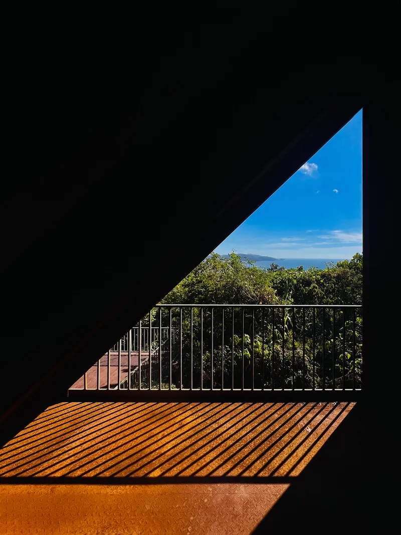 Triangular opening framing a metal railing and ocean view with wooden deck in sunlight