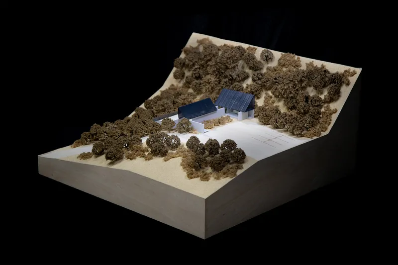 Physical model showing two volumes with sloped roofs set within a hillside landscape