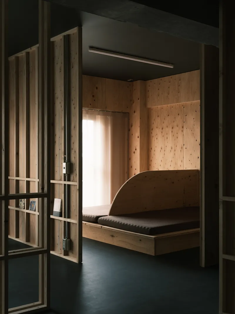 Timber-lined sleeping alcove with built-in bench and glazed door softly backlit by daylight