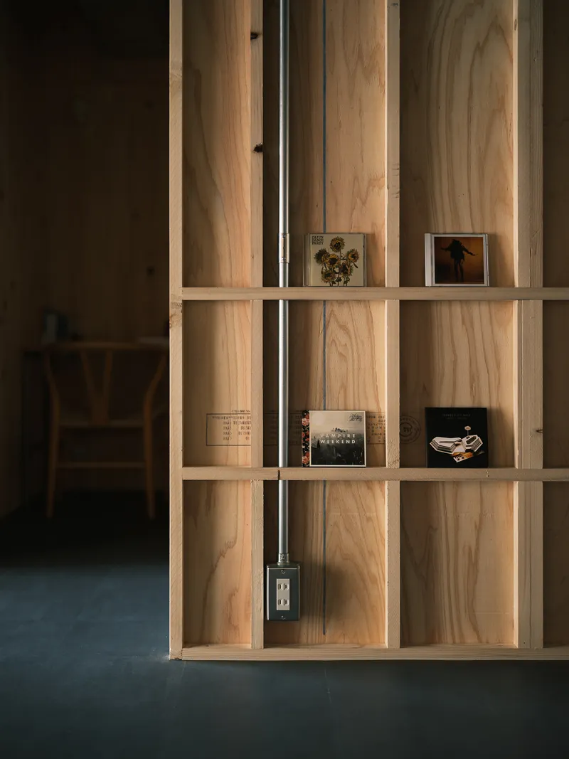 Plywood shelving unit with vertical conduit and electrical outlet displaying small framed photographs