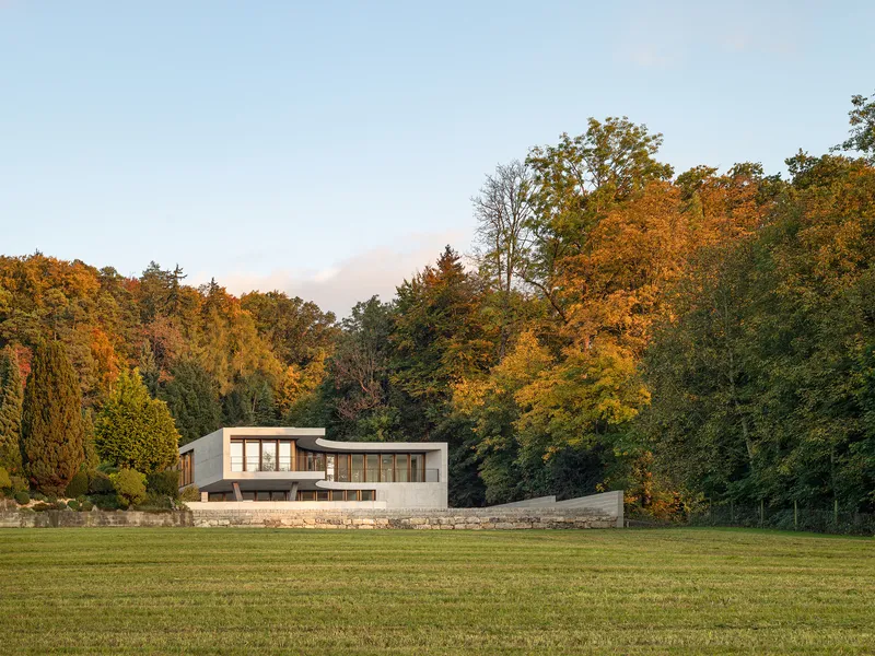 Distant view of the concrete and timber residence across an open lawn with autumn trees