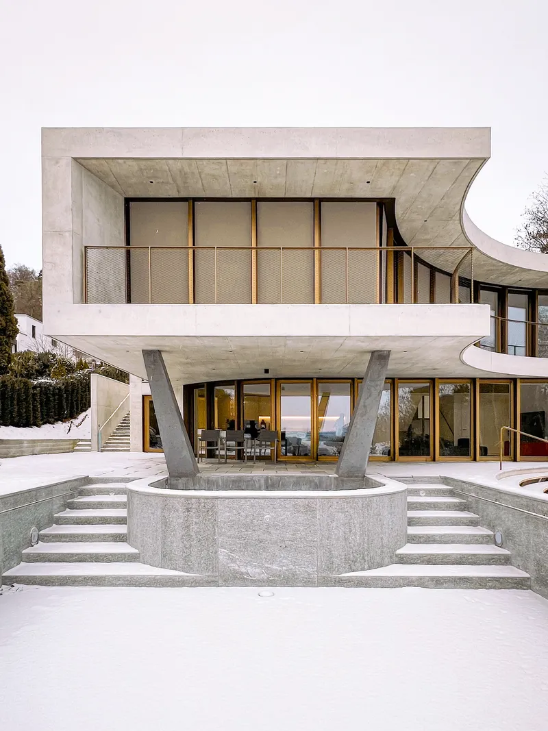 Curved concrete pool basin with symmetrical stepped access leading to cantilevered terrace and glazed lower level