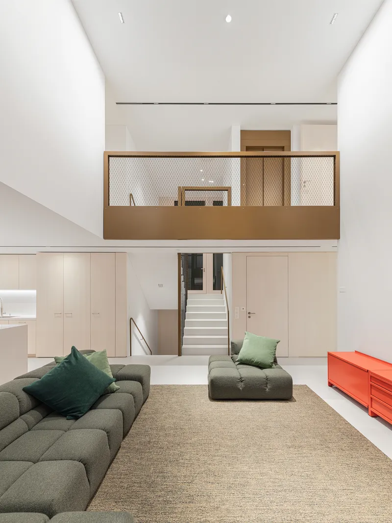 Double-height living room with suspended timber and mesh balcony above built-in storage and stair