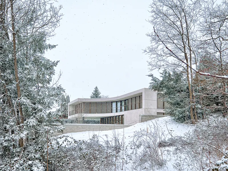 View of the curved concrete roof and timber screens from snow-covered garden with bare trees