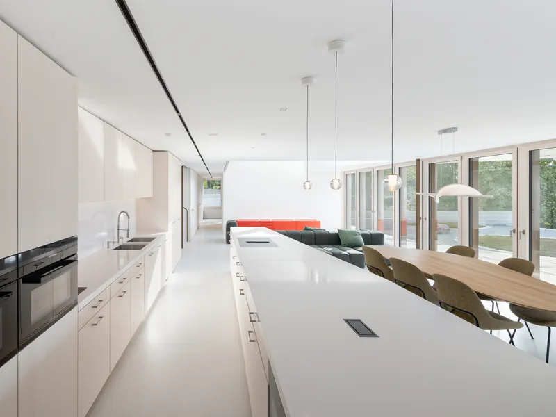 Open kitchen with white island and pendant lights extending into dining area with garden doors