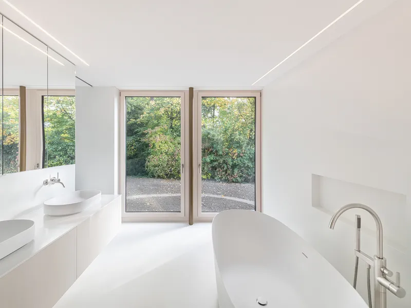 White bathroom with freestanding tub and timber-framed doors opening to garden with trees