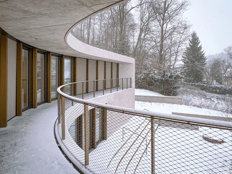 Curved concrete balcony with mesh railing and vertical timber screens during winter snowfall