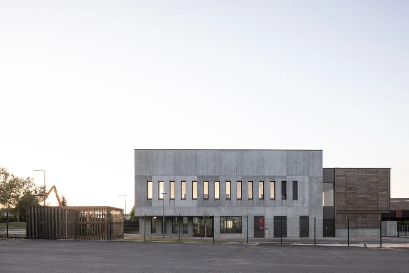 Street-facing facade with vertical slit windows and timber-screened entrance gate at dusk