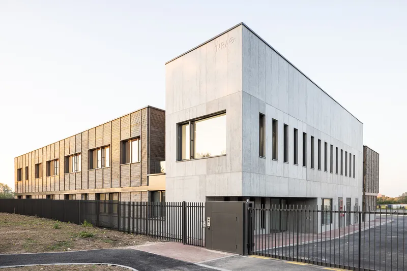 Corner view showing the concrete upper volume with vertical fenestration and dark metal perimeter fence