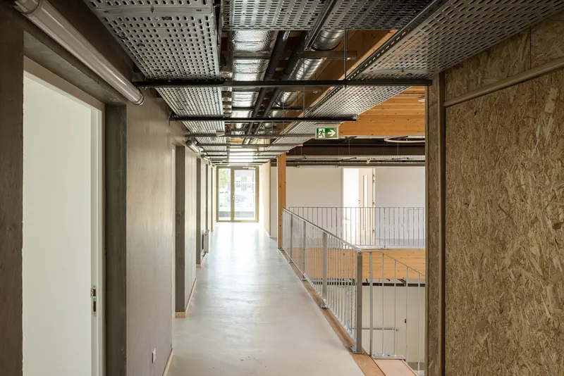 Interior corridor with exposed perforated metal ceiling, oriented strand board walls and steel guardrail overlooking lower level