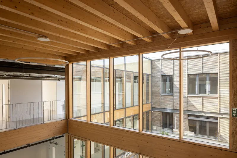 Glazed interior courtyard facade with exposed timber beams and plywood panels framing views between floors