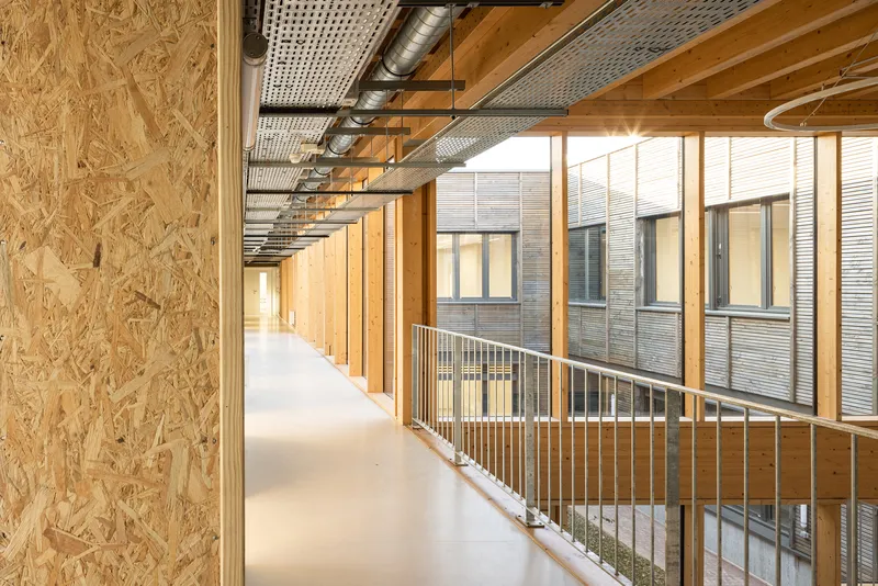 Interior corridor with exposed oriented strand board walls, timber guardrail, and exposed ductwork overhead