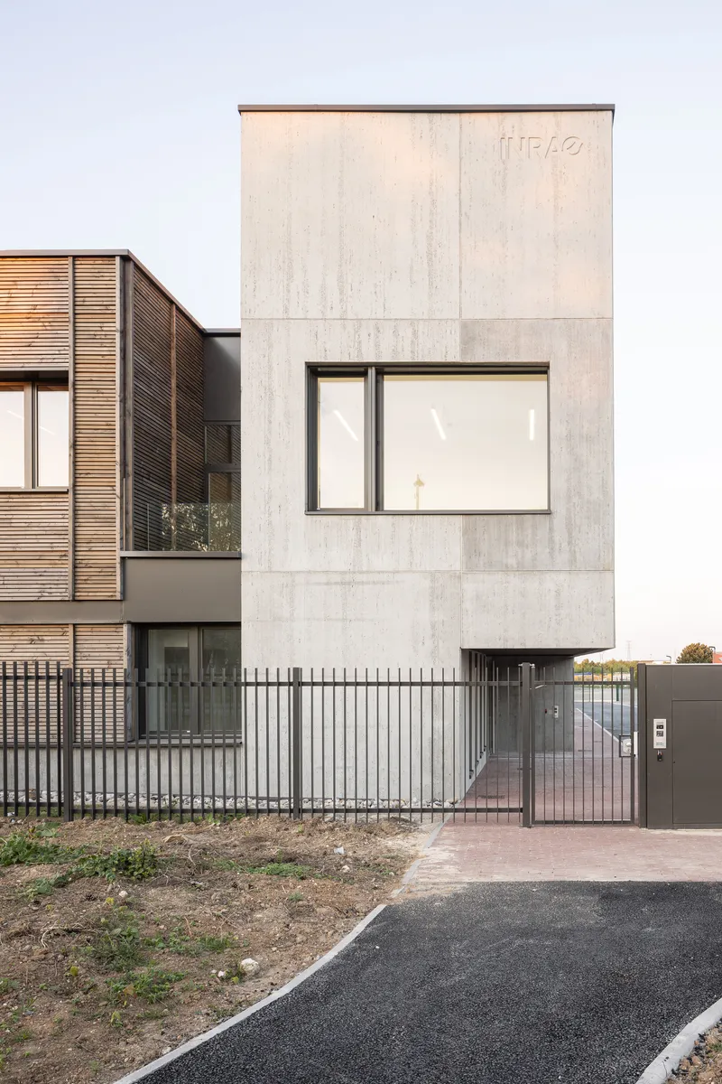 Street view of the concrete facade with a single window next to a timber-clad volume and metal fence