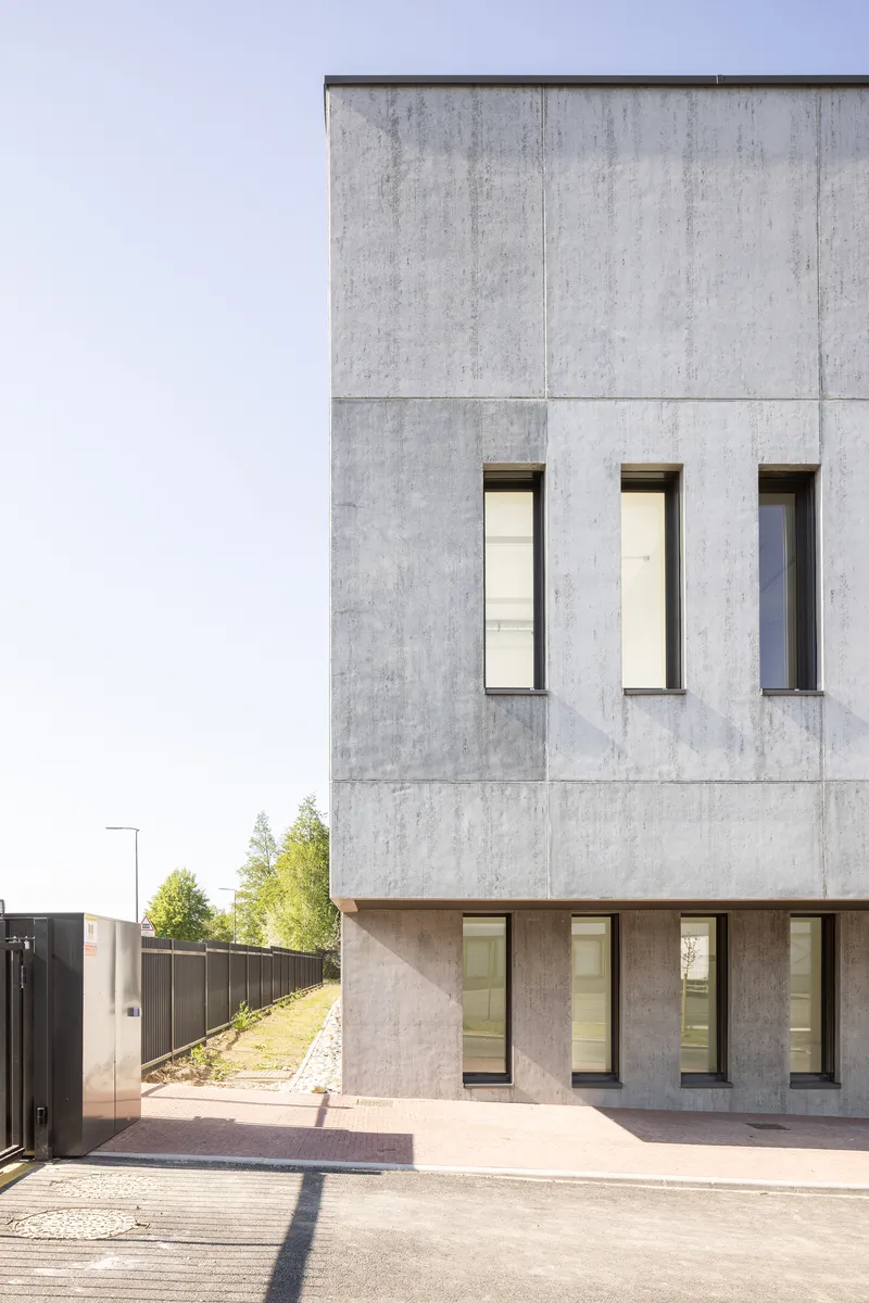 Concrete facade with three vertical windows above a recessed timber-clad ground floor entry in morning light