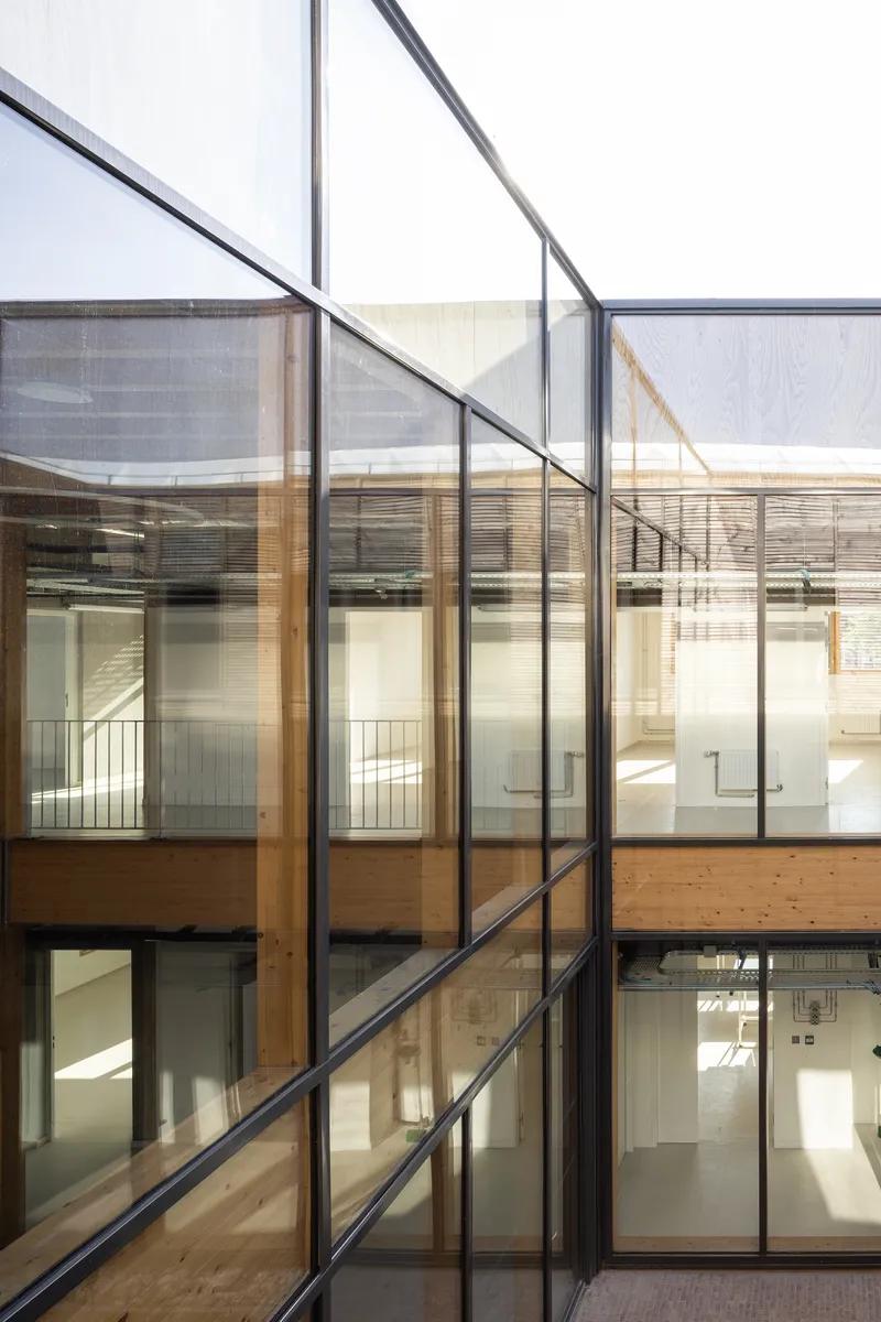 Interior courtyard showing glazed facades with timber frames and exposed timber beams spanning between levels in sunlight