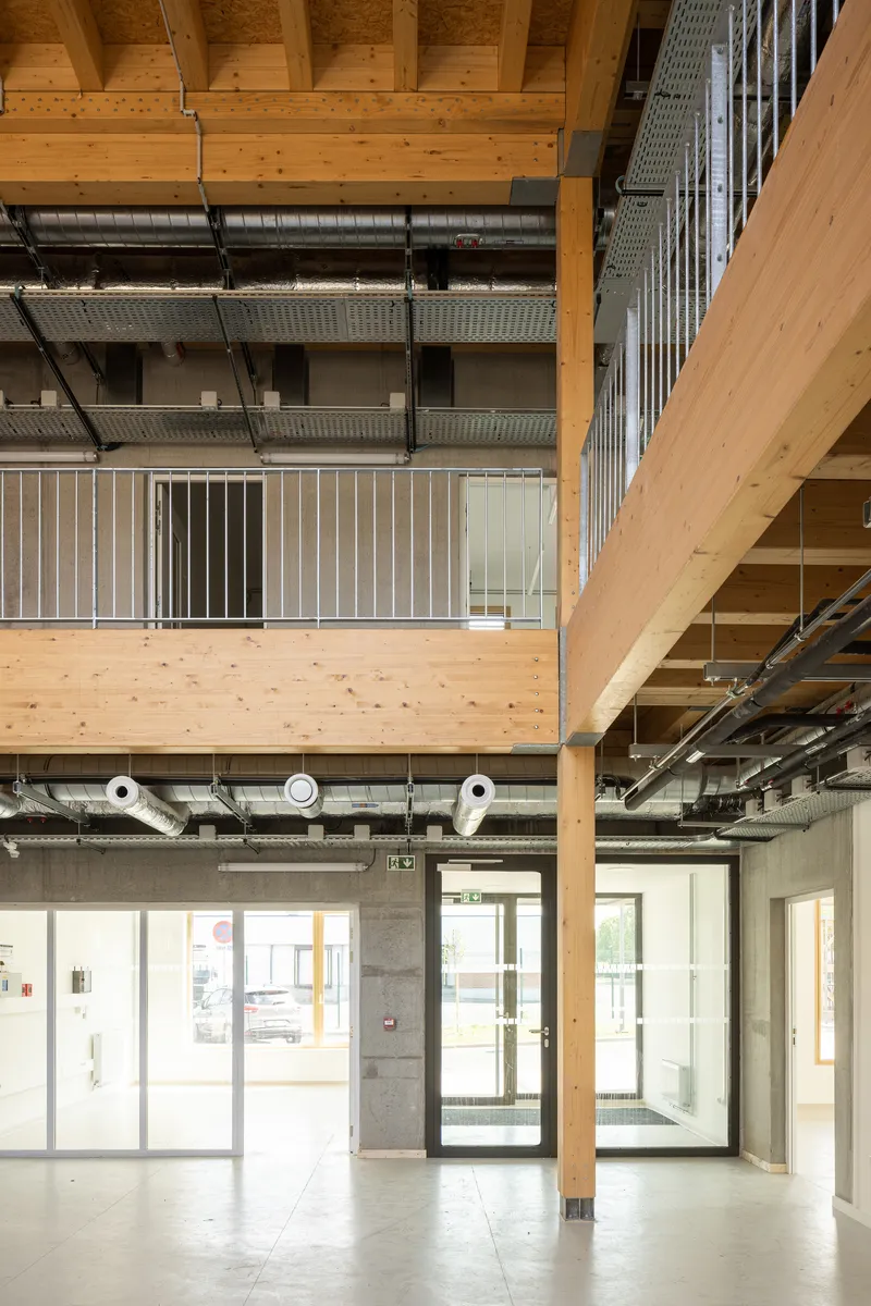 Double-height interior atrium with exposed timber beams and metal ductwork spanning across levels
