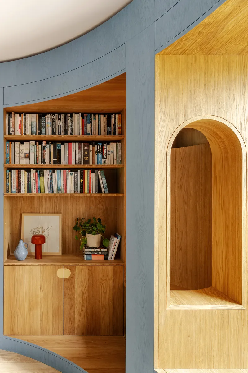 Detail of timber bookshelf niche and arched reading alcove set within curved blue paneled wall