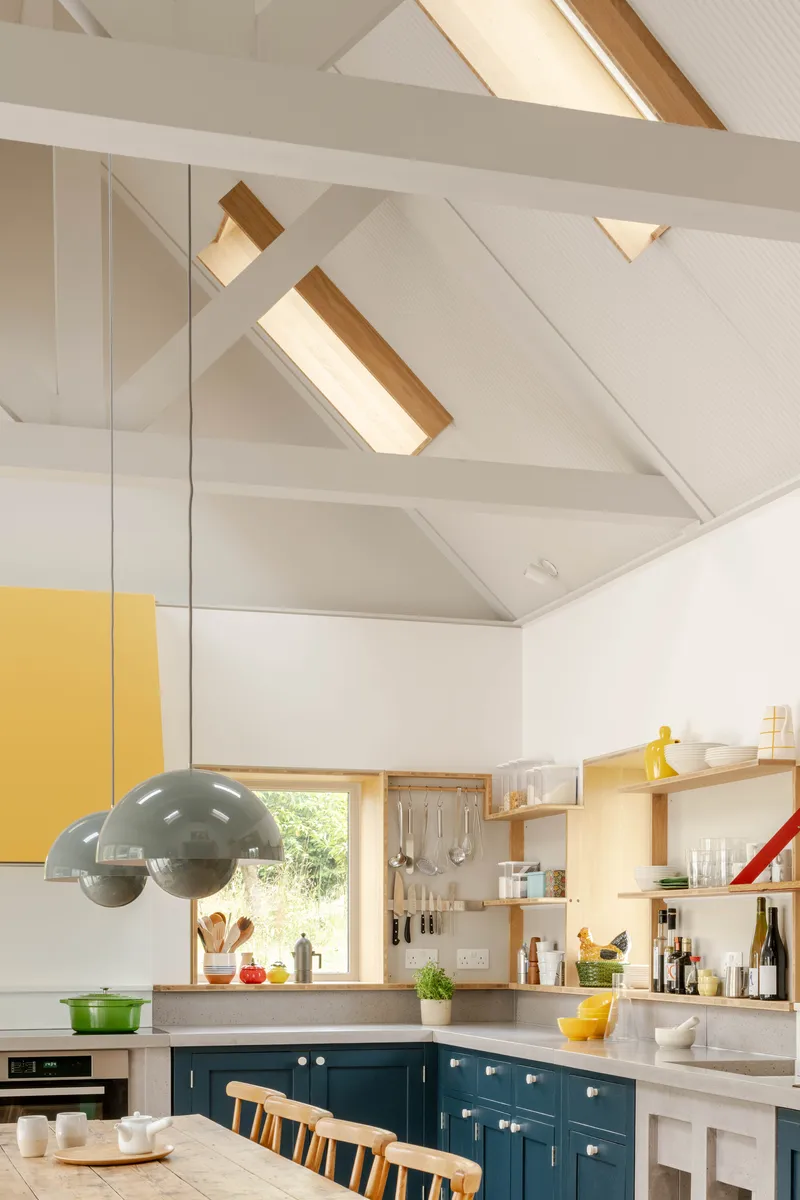Kitchen with vaulted white ceiling, skylights, teal cabinetry and yellow pendant cabinet above island
