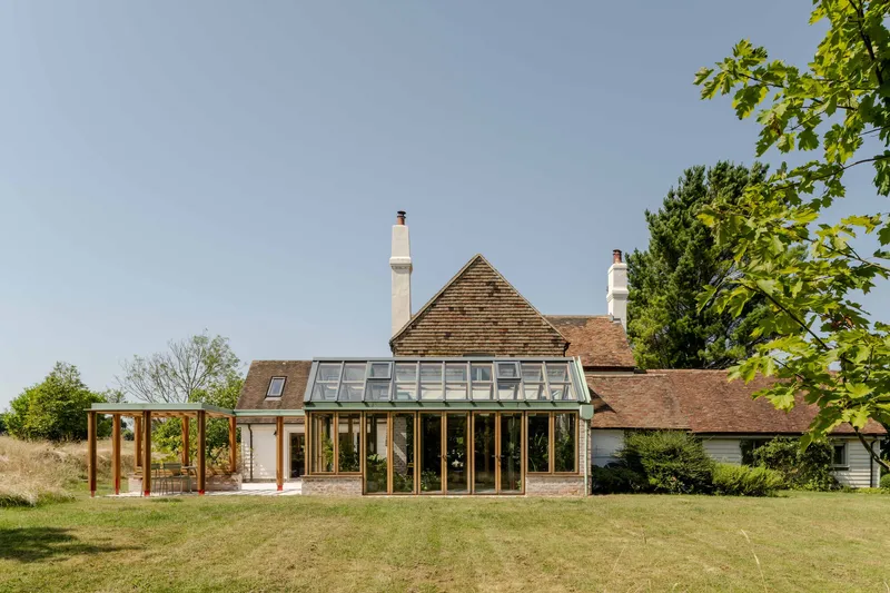 Garden view of the glazed conservatory extension connecting to the tiled-roof house in summer