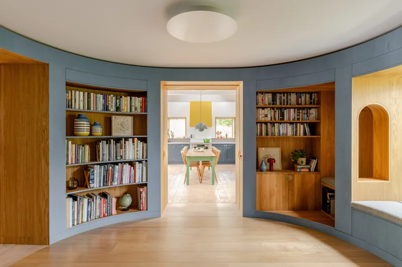 Curved hallway with built-in timber bookshelves set into painted blue walls and doorway beyond