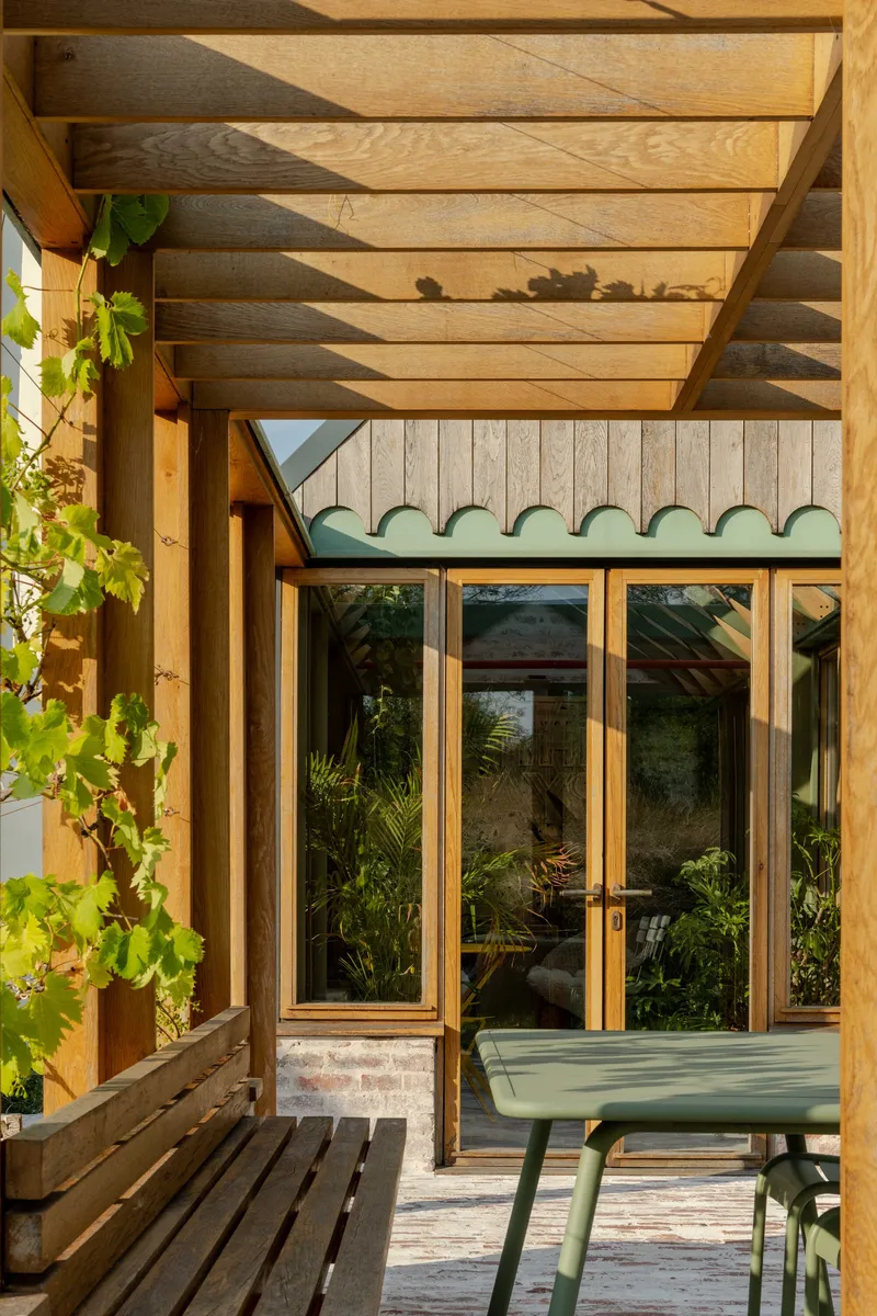 Covered porch with timber rafters, scalloped green trim above glazed doors and afternoon sunlight filtering through