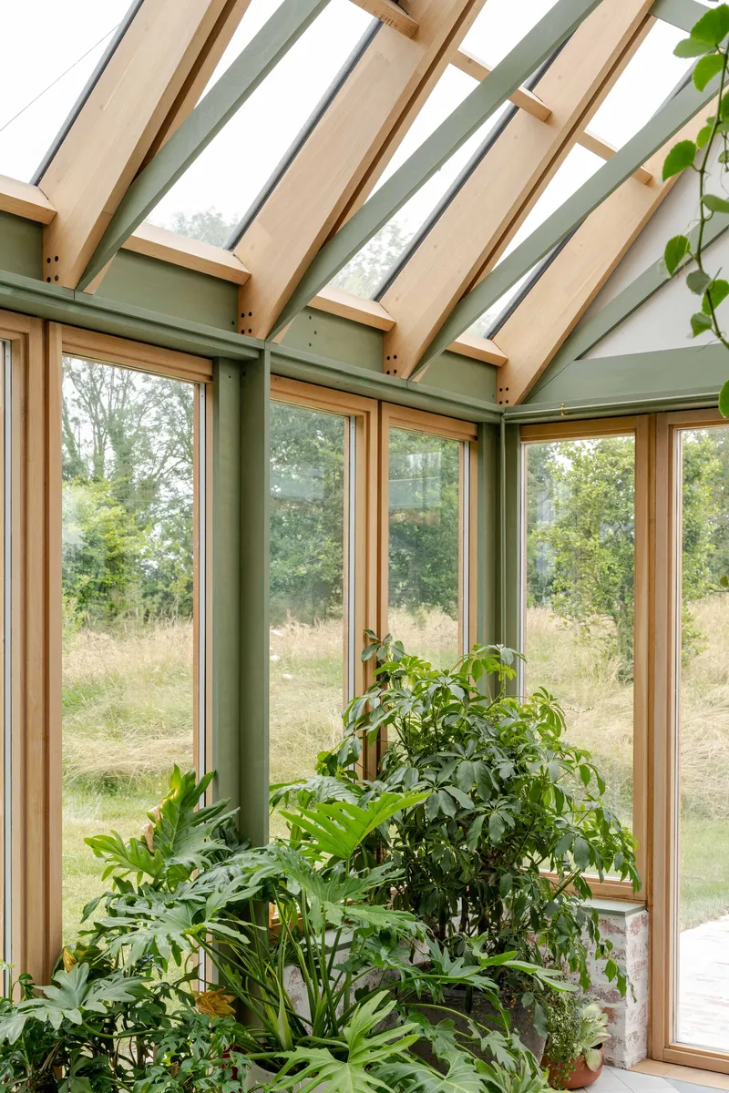 Corner conservatory interior with timber-framed windows, green posts and an array of potted plants
