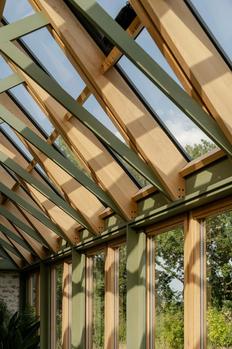 Angled timber rafters and glass roof panels creating diagonal shadow patterns on green-painted columns