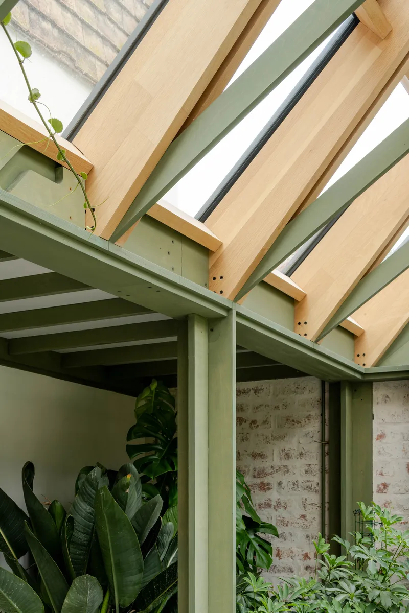 Overhead view of timber rafters and sage green steel beams with climbing vines and planted courtyard below