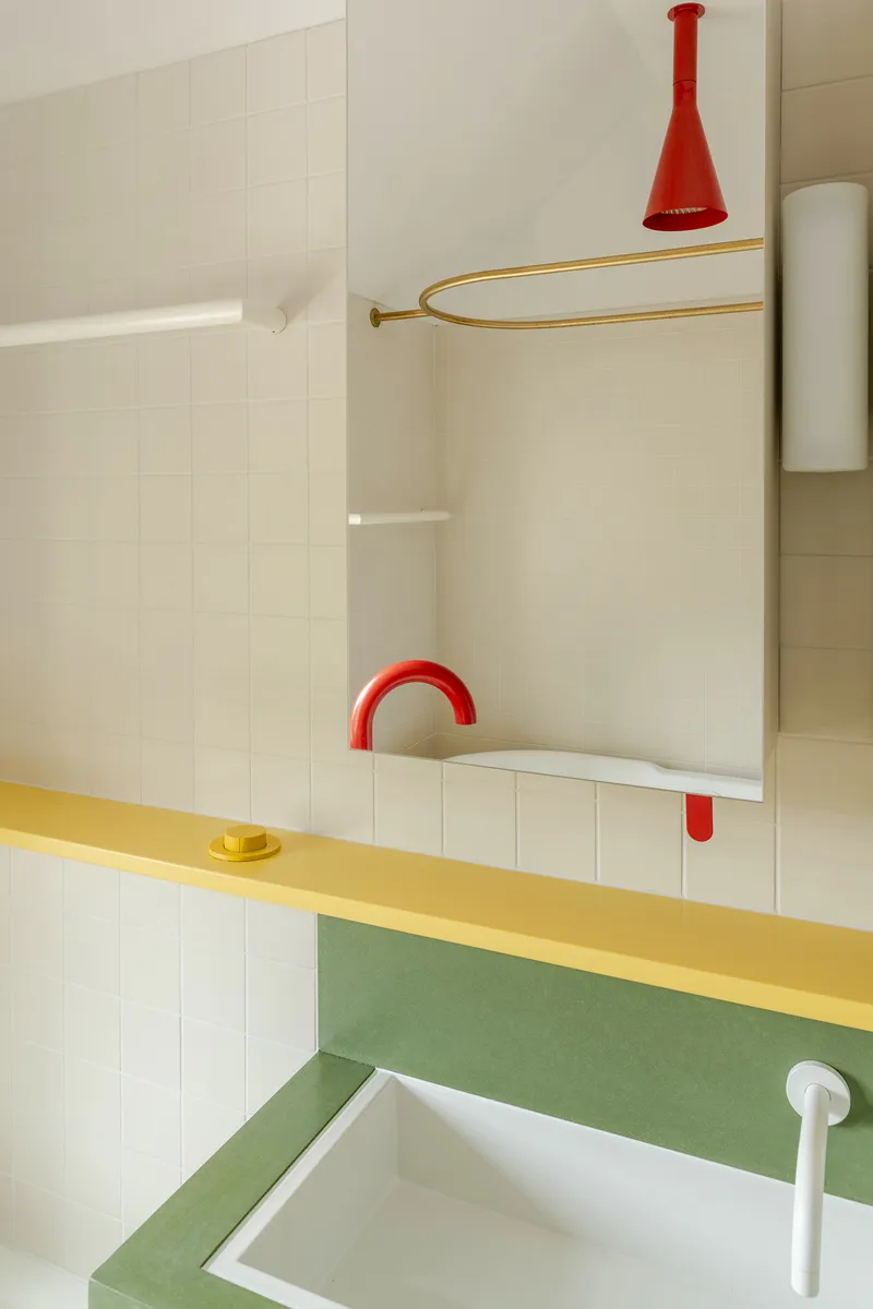 Bathroom vanity with yellow counter, green backsplash, red arched faucet and brass shower curtain rail