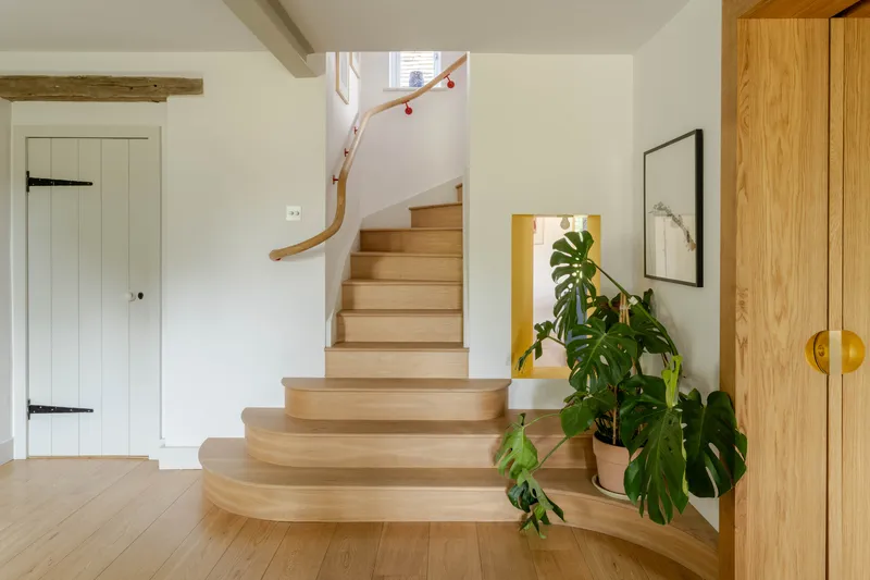 Timber staircase with curved treads and handrail ascending past a monstera plant and yellow-edged opening