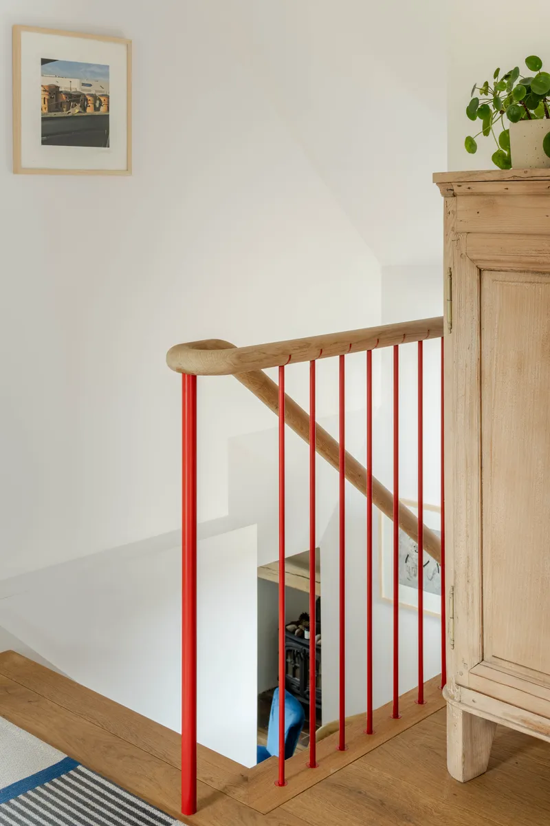 Landing balustrade with red vertical balusters, timber handrail and newel post against a white wall