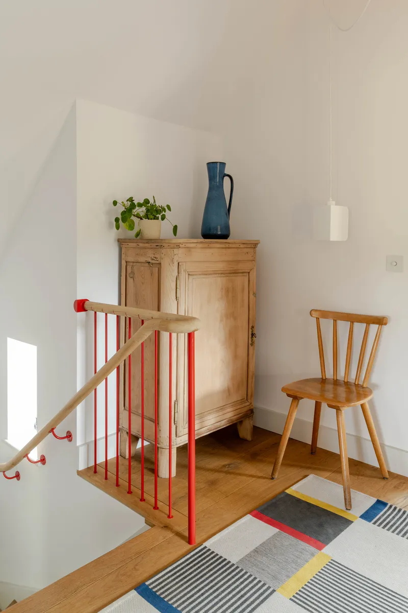 Upper landing with red steel balustrade, oak armoire, and patterned rug in afternoon light